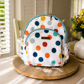 Handmade colorful polka dot mini backpack with boutique-style craftsmanship displayed on a wooden table beside decorative flowers indoors.