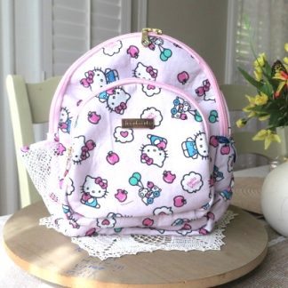 Handmade pink cute mini backpack with colorful character-inspired fabric displayed on a wooden table beside decorative flowers indoors.