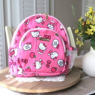 Handmade bright pink cute mini backpack with playful character-inspired fabric displayed on a wooden table beside decorative flowers indoors.
