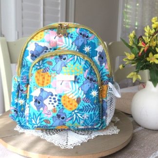 Handmade tropical paradise mini backpack with colorful island-inspired artwork displayed on a wooden table beside decorative flowers indoors.