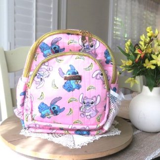 Handmade pink tropical cute mini backpack with colorful island-inspired artwork displayed on a wooden table beside decorative flowers indoors.