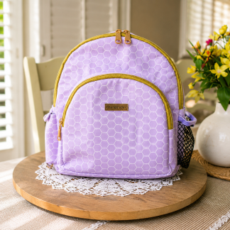 Handmade lavender boutique mini backpack with elegant geometric fabric displayed on a wooden table beside decorative flowers indoors.
