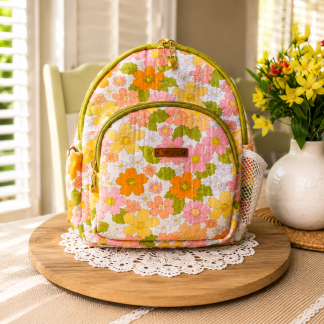 Handmade vintage floral mini backpack with colorful retro-inspired flower fabric displayed on a wooden table beside decorative flowers indoors.