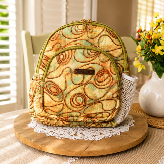 Handmade elegant swirl mini backpack with artistic earthtone fabric displayed on a wooden table beside decorative flowers indoors.
