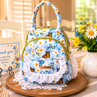 Handmade blue daisy mini backpack crafted from quilted cotton with butterfly print, lace trim, and multiple storage pockets displayed on a wooden stand.