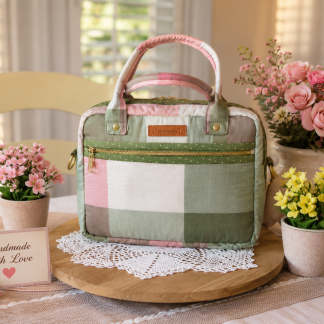 Handmade green and pink plaid iPad bag with front zipper pocket displayed on a wooden tray surrounded by flowers.