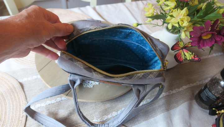 Handmade gray Shoulder Bag and Handbag Combo with adjustable shoulder strap and gold zipper displayed on a wooden tray with flowers in a warm home setting.