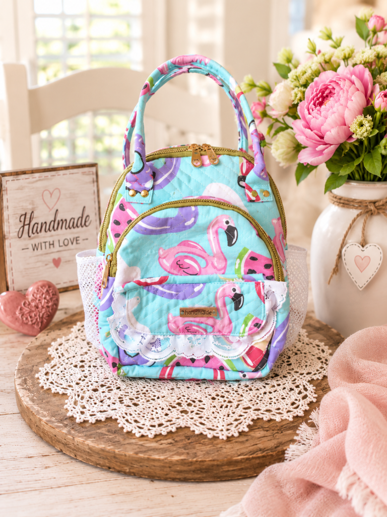 Handmade pink flamingo backpack with aqua quilted canvas, decorative white lace and gold-tone zippers.
